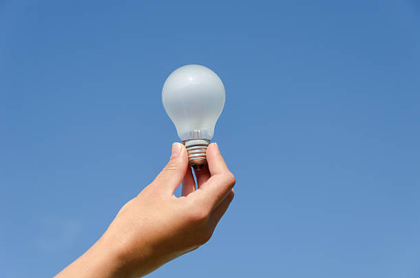 hand hold light bulb on blue sky background stock photo