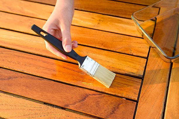 hand holding a brush applying varnish on a garden table stock photo