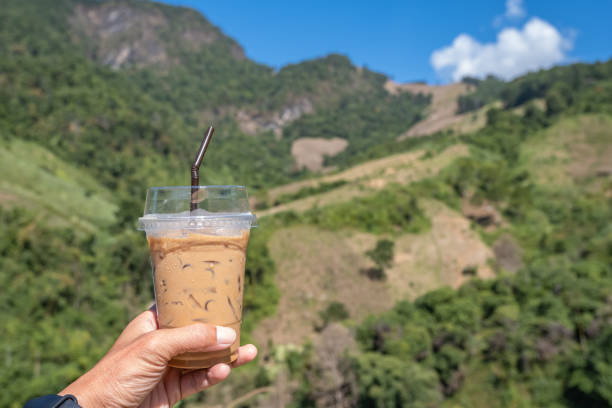 Hand holding a glass of cold espresso coffee Background blurry views tree and mountain stock photo