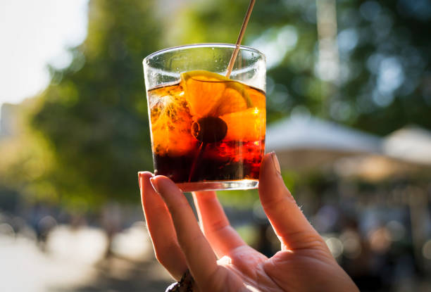 hand holding a glass of vermouth outdoors in the sunlight This image capture shows a hand holding a glass of refreshing vermouth alcoholic beverage in outdoors in the sunlight. vermouth stock pictures, royalty-free photos & images