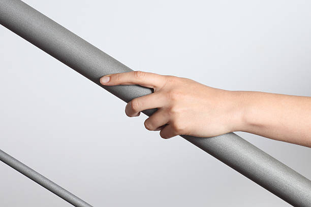 Hand holding a gray matte handrail going up, gray background Woman hand using a railing to go upstairs with a light grey background bannister stock pictures, royalty-free photos & images