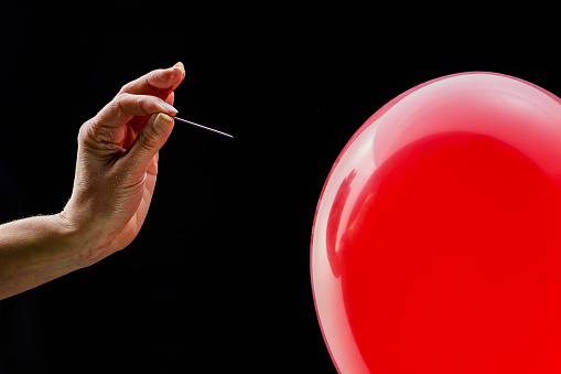 Hand holding a needle next to a red balloon