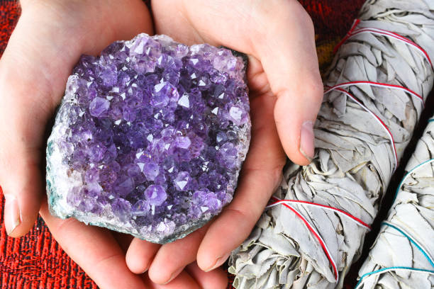 Hand Holding Amethyst Geode Cluster A close up image of a hand holding beautiful purple amethyst cluster next to two white sage bundles. amethyst stock pictures, royalty-free photos & images