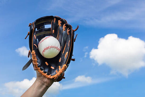 Hand holding baseball in glove with blue sky stock photo