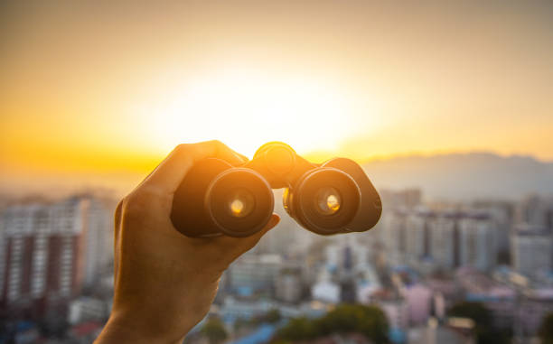 Hand holding black binoculars at city sunset Hand holding black binoculars at city sunset binoculars stock pictures, royalty-free photos & images