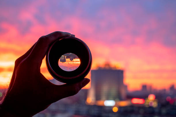 hand holding camera lens, looking at scenics of glowing clouds at sunset stock photo