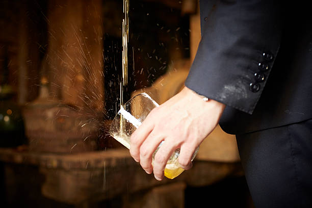 Hand holding cider glass that is being poured Detail of a hand holding a glass of cider that is being poured. The man who is pouring is wearing a black suit and the background, out of focus, is warm tones. The stream of cider splashes and the droplets are captured by the photographer's camera lens. Horizontal format. cider stock pictures, royalty-free photos & images