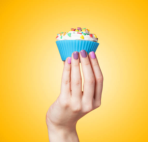 Hand holding cupcake on yellow background stock photo