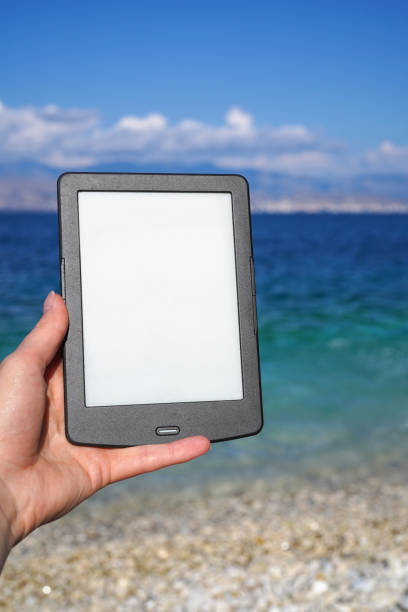 hand holding e-book reader on the beach stock photo