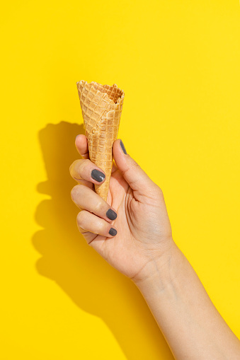 Hand holding empty icecream cone on yellow background