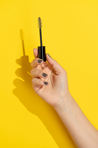Hand holding mascara brush on yellow background