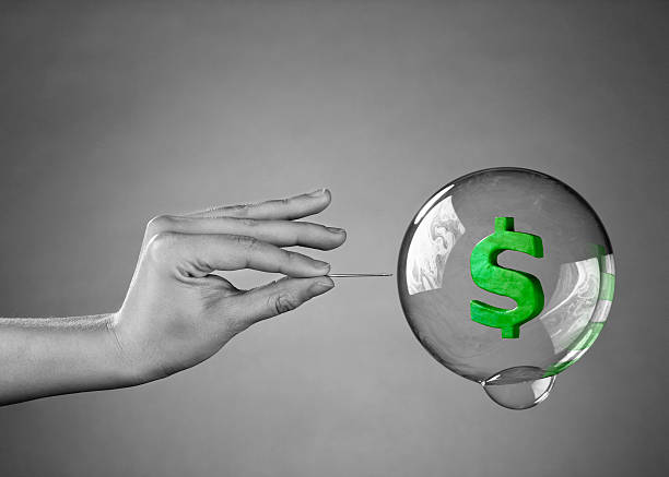 Hand holding needle about to pop bubble with dollar sign stock photo