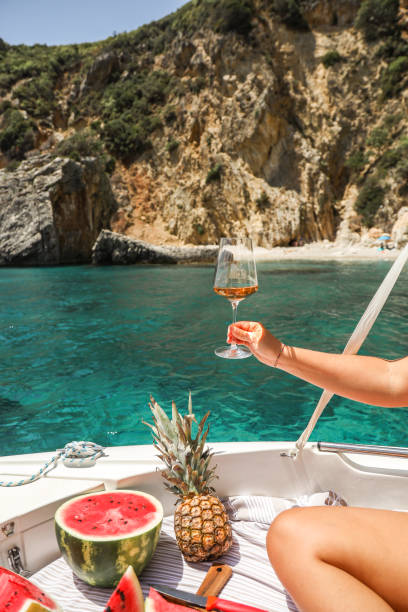 hand holding rosé wine glass in boat with fruit picnic stock photo