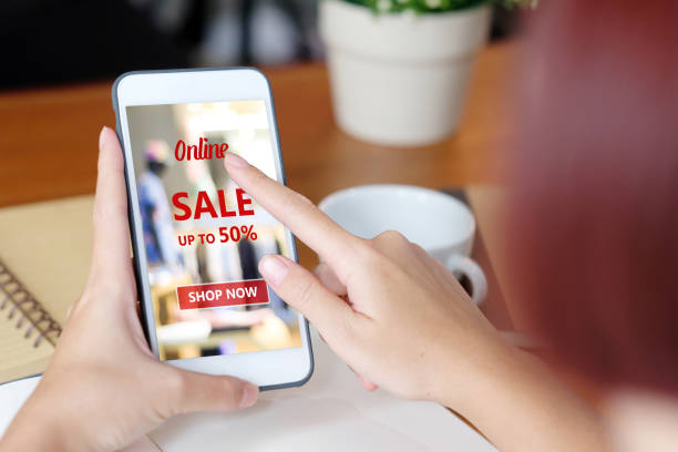 Hand holding smart phone with black friday sale on screen device over blur store background, business and technology, online shopping, digital marketing concept stock photo