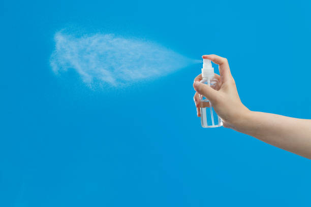 Hand holding spray bottle on blue background Hand holding spray bottle on blue background. spraying stock pictures, royalty-free photos & images