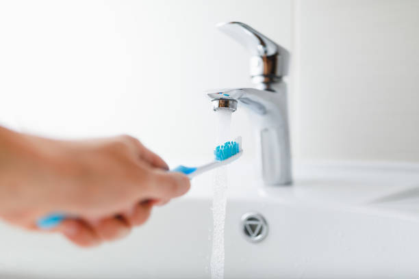 hand holding toothbrush under flowing water from faucet stock photo