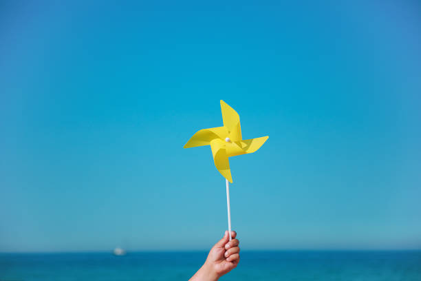 handhaltigen gelben pinwheel im meer - windräder stock-fotos und bilder
