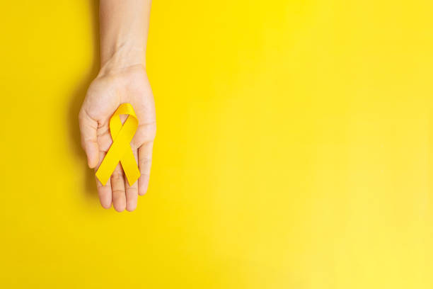 hand holding Yellow Ribbon on yellow background for supporting people living and illness. Suicide prevention day, Sarcoma cancer and Childhood Cancer Awareness month concept stock photo