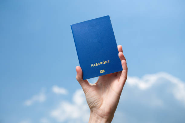 Hand holds passport on background of blue sky with clouds. Travel concept stock photo