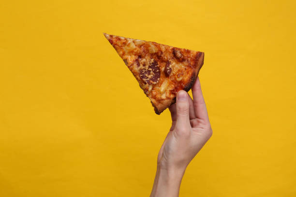 Hand holds piece of homemade pizza on a yellow background stock photo
