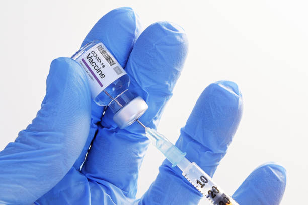 Hand in gloves holding and transferring COVID-19 vaccine from vial to syringe stock photo