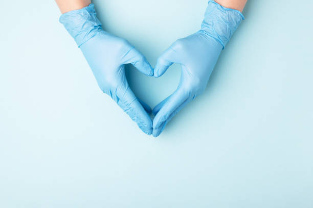 Hand in medical gloves. Doctor's hands in medical gloves in shape of heart on blue background with copy space. care stock pictures, royalty-free photos & images