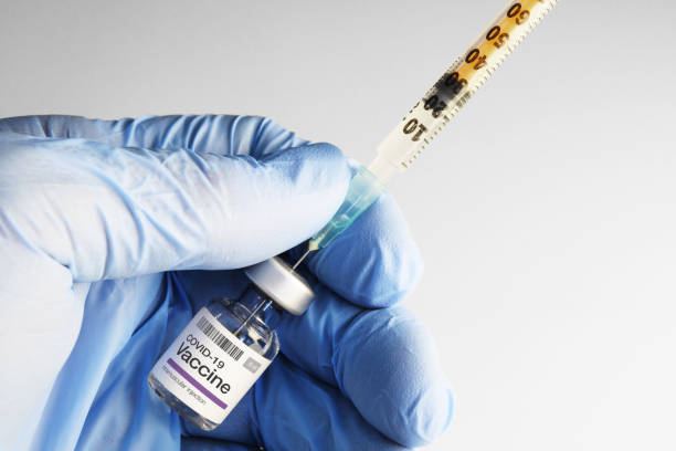 Hand in nitrile gloves holding COVID-19 vaccine preparing syringe for injection stock photo