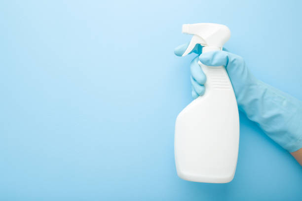 Hand in rubber protective glove holding white spray bottle. Detergent for different surfaces in kitchen, bathroom and other rooms. Closeup. Empty place for text or logo. Light pastel blue background. Hand in rubber protective glove holding white spray bottle. Detergent for different surfaces in kitchen, bathroom and other rooms. Closeup. Empty place for text or logo. Light pastel blue background. purity stock pictures, royalty-free photos & images
