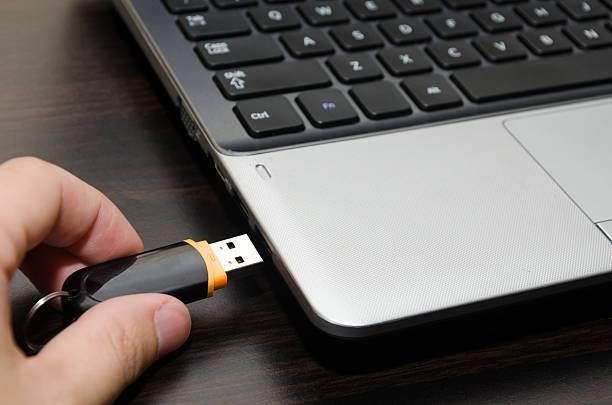 Hand inserting USB flash drive into laptop computer port close-up stock photo