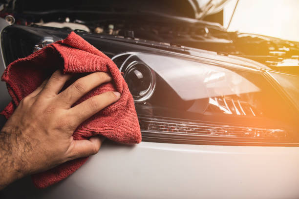 Hand is cleaning car headlight with a using red microfiber cloth. stock photo