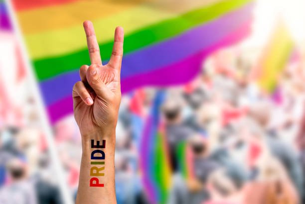 hand makes peace sign in front of a rainbow flag Supporting hand makes peace sign in front of a rainbow flag flying on the sidelines of a summer gay pride parade with copy space nyc pride parade stock pictures, royalty-free photos & images