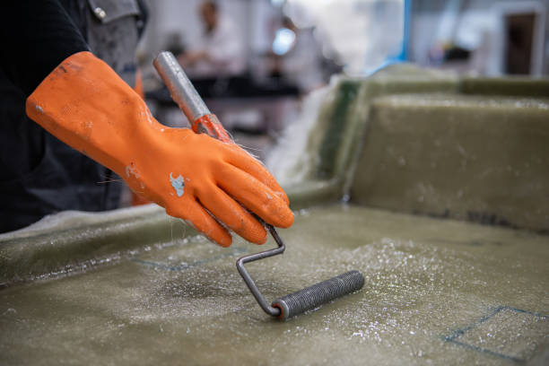 Hand of a fibreglass factory worker in a glove rolling solution Hand of a factory worker in a glove rolling chemical solution with a tool on the fiberglass mold fibreglass stock pictures, royalty-free photos & images