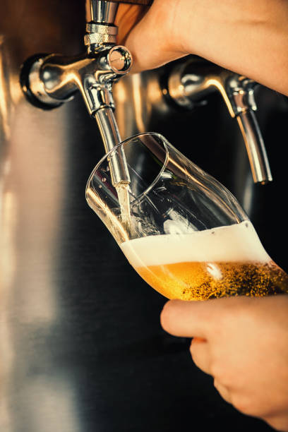 la mano del camarero verter una cerveza lager beer in tap - mano agarrando botella de cerveza y taza fotografías e imágenes de stock