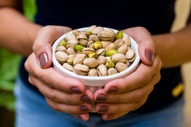Hand of brunette model holding white pot with pistachio stock photo