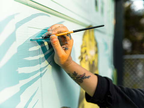 Close up of hand of Female mural artist creating art on the garage door of the private home in the city.