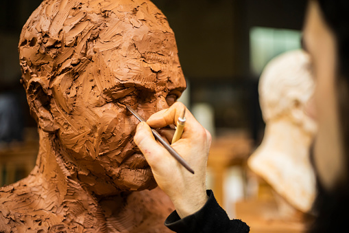 Hand of sculptor finishing a clay head eye in an art studio