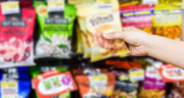 hand of woman choosing or taking sweet products, snacks on shelves in convenience store stock photo