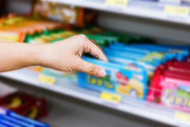 hand of woman choosing or taking sweet products, snacks on shelves in convenience store stock photo