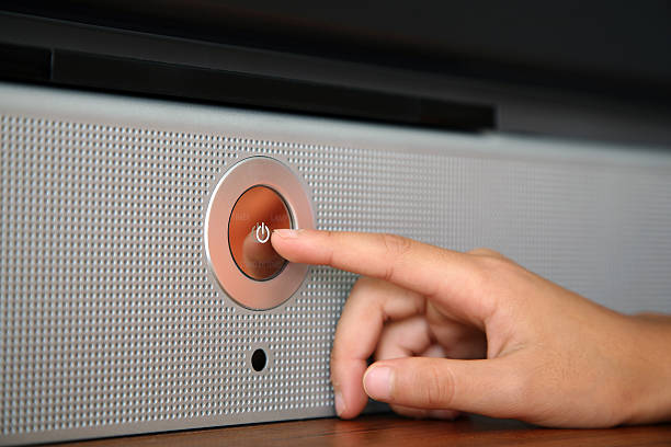 A hand pressing a silver power button on a speaker stock photo