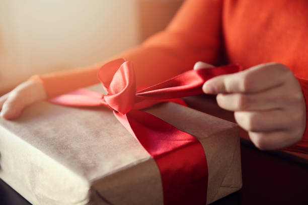 Hand pulls red ribbon on a gift wrapped in brown paper Box - Container, Holiday - Event, Event, Gift Box, Human Hand, Valentine's Day,  noel, New years birthday present stock pictures, royalty-free photos & images