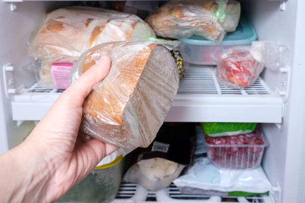 A hand putting a package of brown bread in reserve on a shelf of a home freezer, long life food storage concept stock photo