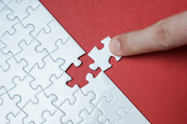 Hand putting piece of white jigsaw puzzle on red background. Team business success partnership or teamwork. stock photo
