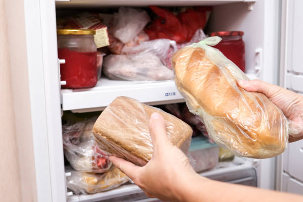 A hand putting two loafs of wheat and brown bread in reserve on a shelf of a home freezer, long life food storage concept stock photo