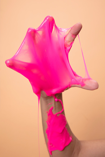 Neon pink slime toy in woman hand on orange pop art background.