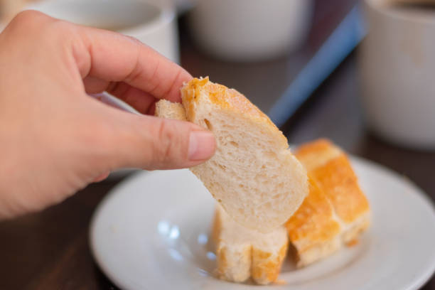 hand taking a piece of bread in restaurant for breakfast on white plate stock photo