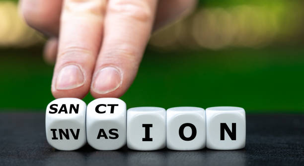 Hand turns dice and changes the word invasion to sanction. stock photo