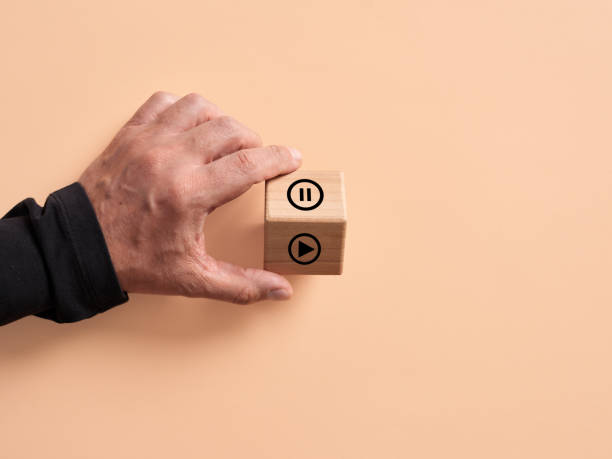 Hand turns the wooden cube with the play and pause symbols. stock photo
