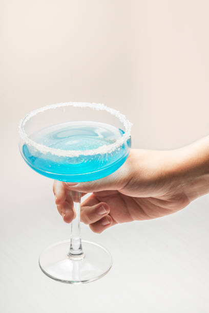Hand with a glass of cocktail in blue on a light background stock photo