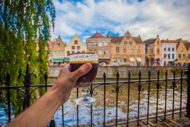 Hand with beer glass in Brugge Full glass of beer on Brugge cityscape background. Hand with beer glass in Bruges, Belgium. brugge, belgium stock pictures, royalty-free photos & images