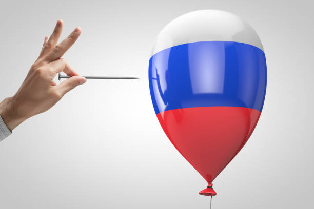 Hand with nail trying to puncture the balloon with Russian symbols stock photo